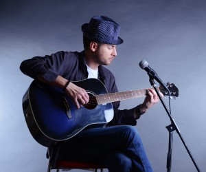 Young musician playing acoustic guitar and singing, on gray back